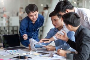 Group of young professionals discussing work around a table with a laptop and documents.