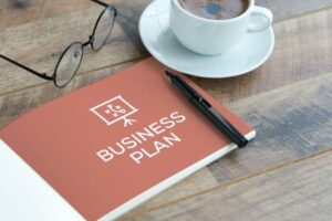 Business plan notebook, coffee, and glasses on a wooden table.