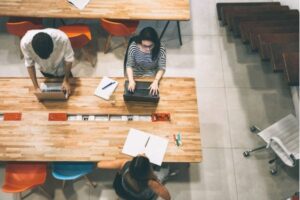 Top view of people working on laptops in a shared workspace.