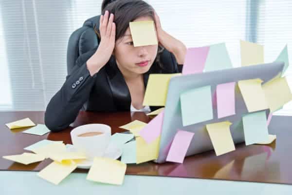 Stressed woman in office surrounded by sticky notes on her laptop.