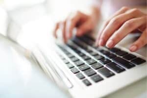 Close-up of hands typing on a laptop keyboard.