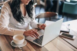 Woman working on a laptop in a cafe with a cup of coffee beside her.