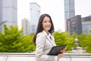 Businesswoman holding a tablet and smiling outdoors in a city setting.