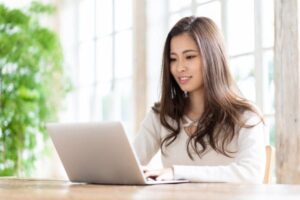 Woman smiling while working on a laptop in a bright indoor setting.