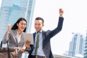 Excited man and woman in business attire cheering outdoors.
