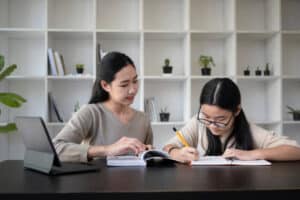 Smiling female tutor helping young student doing homework tutorial