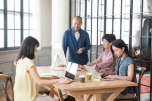 Group of four colleagues working at a wooden table in a bright office.