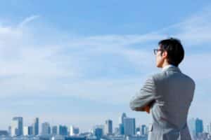 A man in a suit stands confidently in front of a vibrant city skyline during the day.