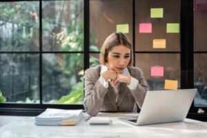 Woman concentrating on laptop at desk with documents.
