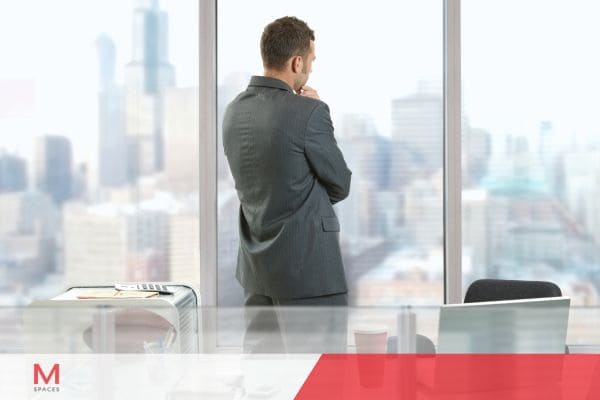 Businessman in suit looking out office window at city skyline.