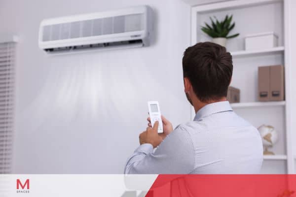 Man adjusting air conditioner with a remote control while working from home during the summer.