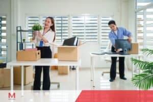 A man and woman are organizing boxes in a private office setup, preparing the space for work activities.