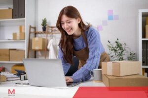 Female small business owner managing online orders and working on a laptop in a home office.