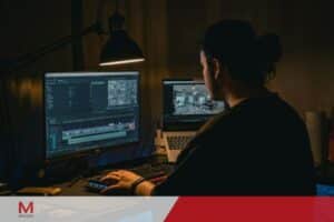 Video editor working late at dual monitor setup with professional editing software in dark studio