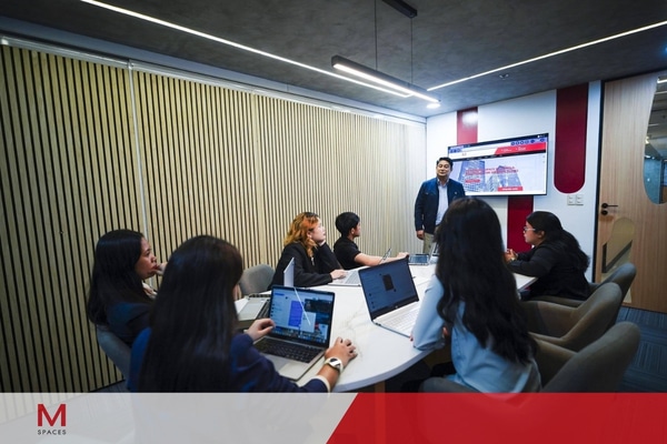 A diverse group of individuals seated at a table, each using laptops, engaged in a collaborative discussion.